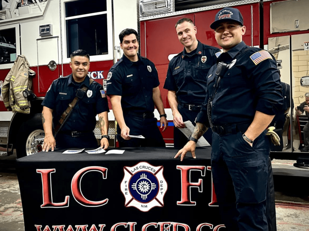 Firefighters at a table with a fire truck in the background